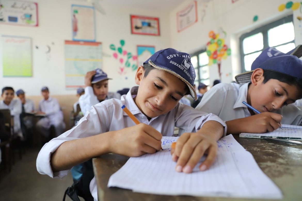Muzzamil Hussain, a grade 7 student at Government High School Dobandi in Haripur, Khyber Pakhtunkhwa, writes in his notebook during class. After two years out of school, he is back to learning and dreaming about his future. Credit: UNICEF/Pakistan/2025/Roham